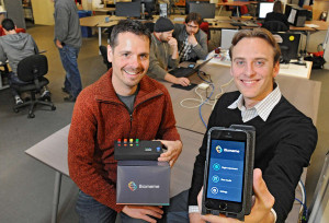 Jesse vanWestrienen (left) of Biomeme shows the company’s diagnostic testing device, while his colleague Max Perelman (right) holds a smartphone that connects to the Biomeme device via bluetooth. (Photo by Clem Murphy and copyright Philly.com.)