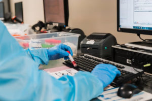 laboratory worker typing at computer with blood sample